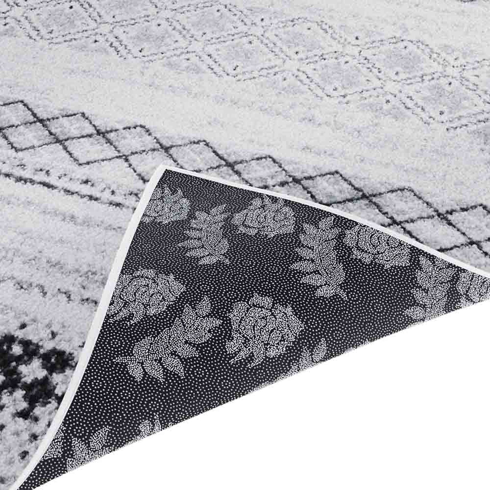 Close-up of Alyne 200x300 Indoor Contemporary Large Floor Rug, showcasing its light pile with a black diamond pattern. Corner lifted to reveal dark, non-slip backing with a dotted floral motif.