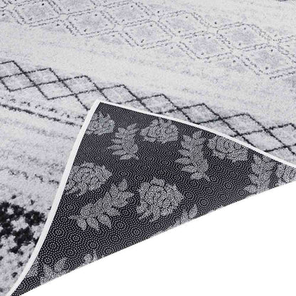 Close-up of Alyne 200x300 Indoor Contemporary Large Floor Rug, showcasing its light pile with a black diamond pattern. Corner lifted to reveal dark, non-slip backing with a dotted floral motif.