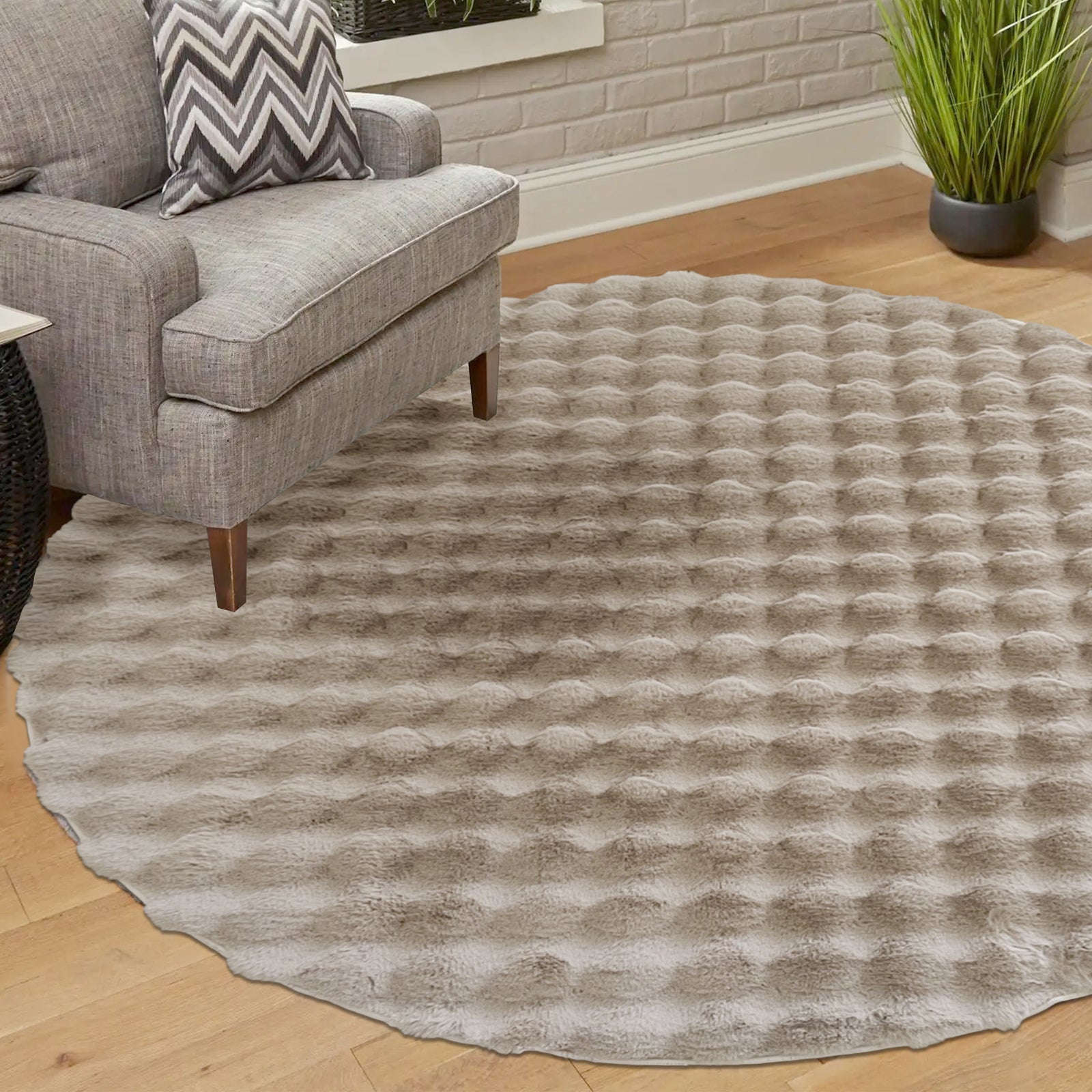Armida 160cm Round Fluffy Faux Fur Bubble Rug in Beige on a light hardwood floor, featuring a plush, waffle-patterned texture beneath a gray armchair with a chevron-pattern throw pillow.