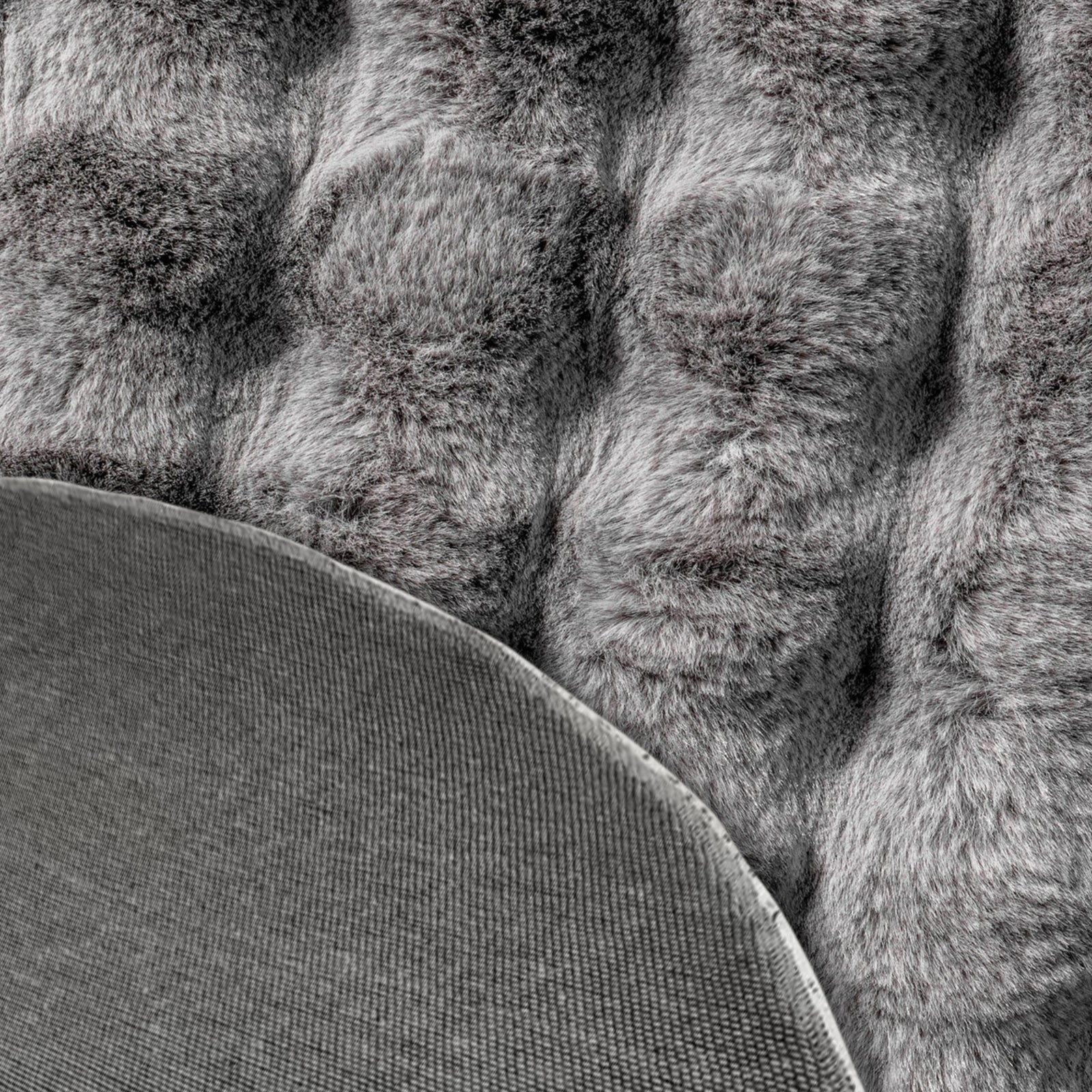Close-up of the Armida 160cm Round Fluffy Faux Fur Bubble Rug in Grey, showcasing its tufted, shaggy texture with a corner flipped, revealing the plain fabric backing.