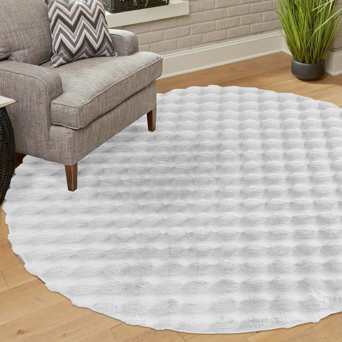 Light-gray armchair with a chevron pillow beside the Armida 160cm Round Fluffy Faux Fur Bubble Rug in White, featuring a plush, dimpled texture, on a light wood floor.