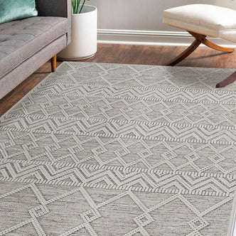 Benita 200x300cm Large Soft Modern Printed Indoor Floor Rug featuring a light geometric pattern, partially under a gray sofa and near a white planter with a houseplant in a cozy living space corner.