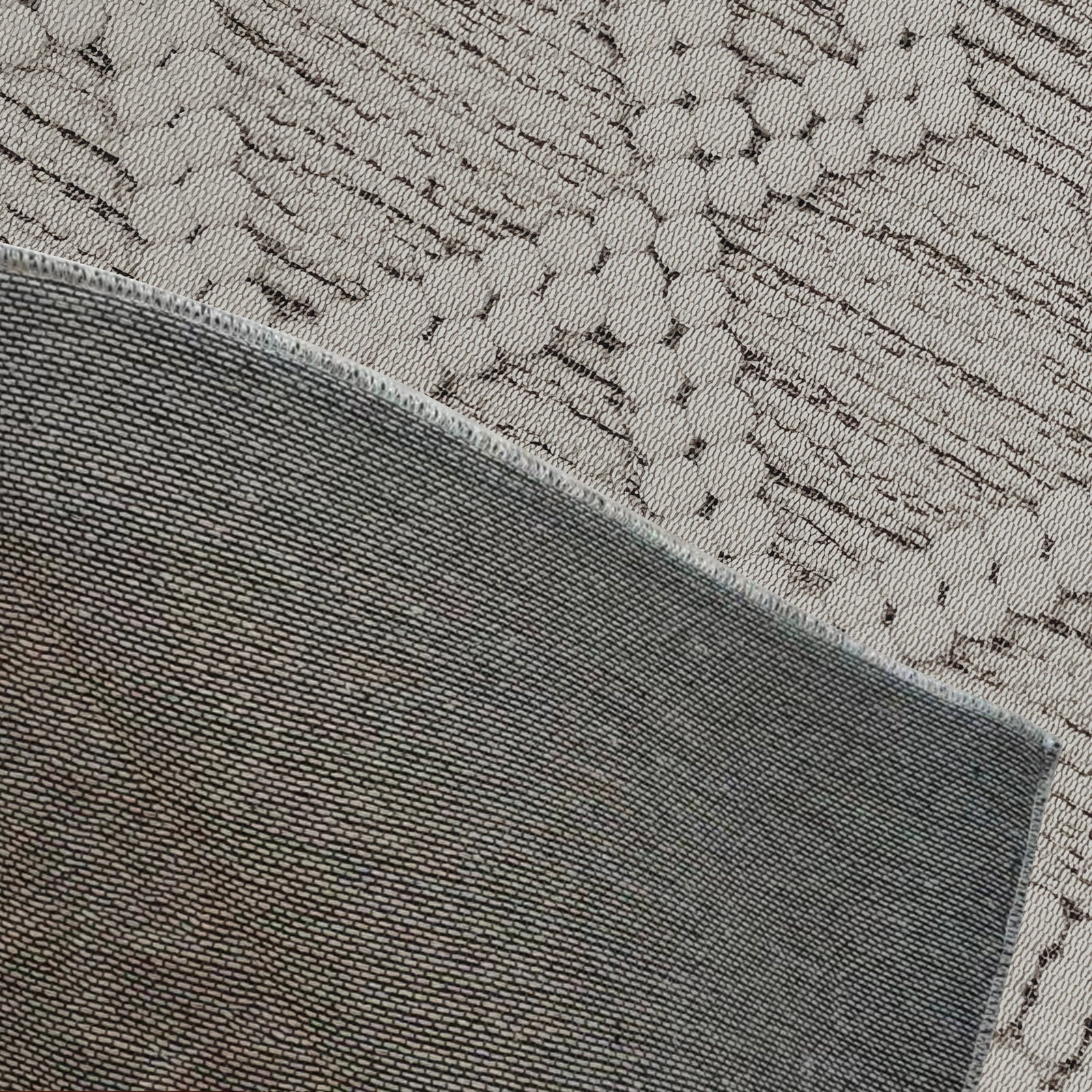 Close-up of the Benita 200x300cm Large Soft Modern Printed Indoor Floor Rug, featuring a folded darker gray-green woven fabric over a lighter gray/beige textile with an abstract linear pattern.