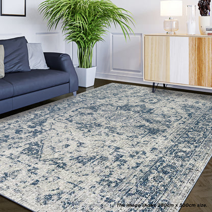 Boda 200x300cm Distressed Persian Silky Indoor Floor Rug in muted blues and off-white, showcased in a minimalist living room with a dark blue sofa and a white planter.