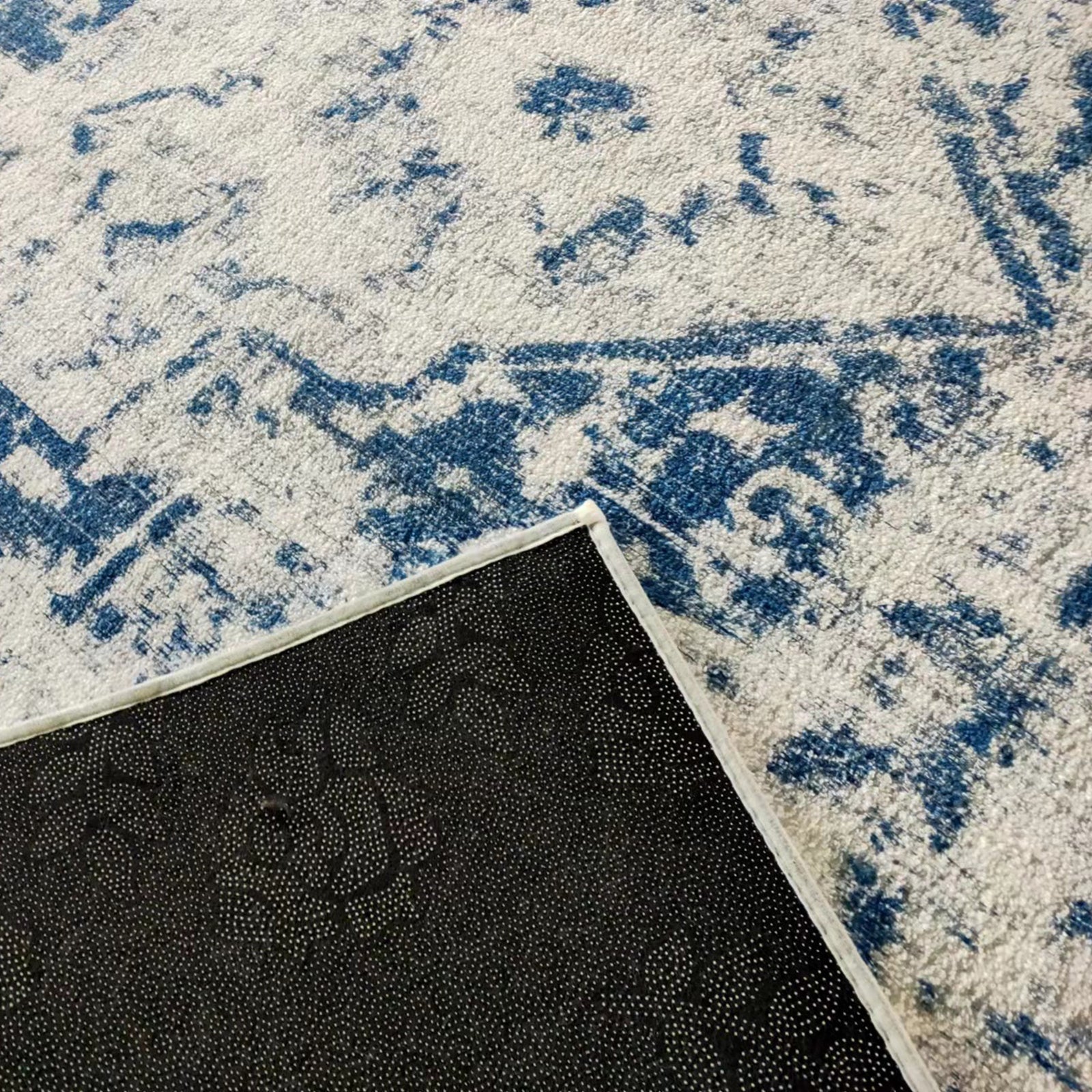 Boda 160x230cm Distressed Persian Silky Indoor Floor Rug features an off-white base with blue abstract patterns, and a visible flipped corner reveals its black, non-slip backing, highlighting functionality and style.