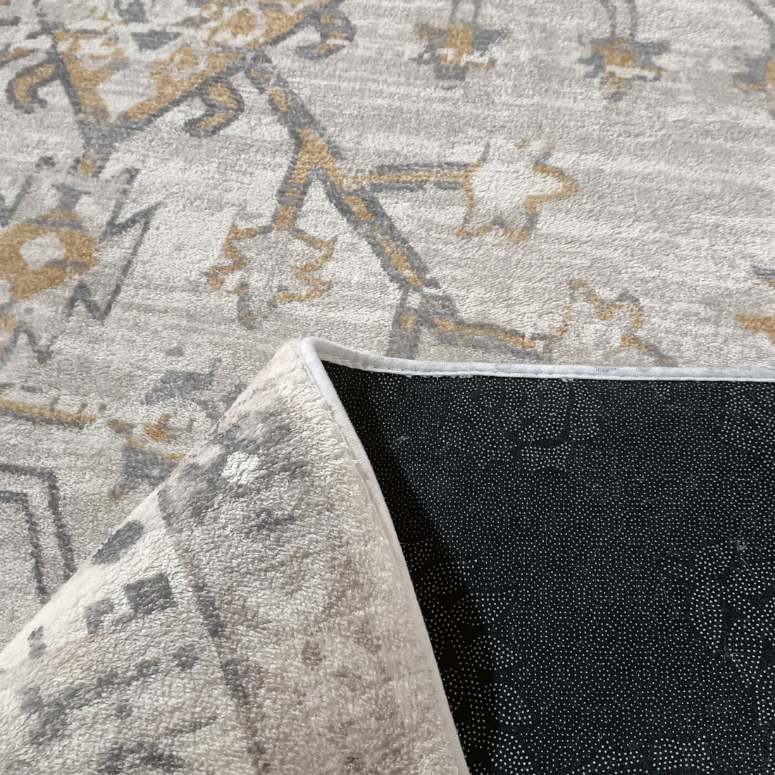 Close-up of Bortan 200x300cm Large Persian Indoor Floor Rug in light gray with muted gold, darker gray pattern, and a flipped corner revealing its black, dotted non-skid backing.
