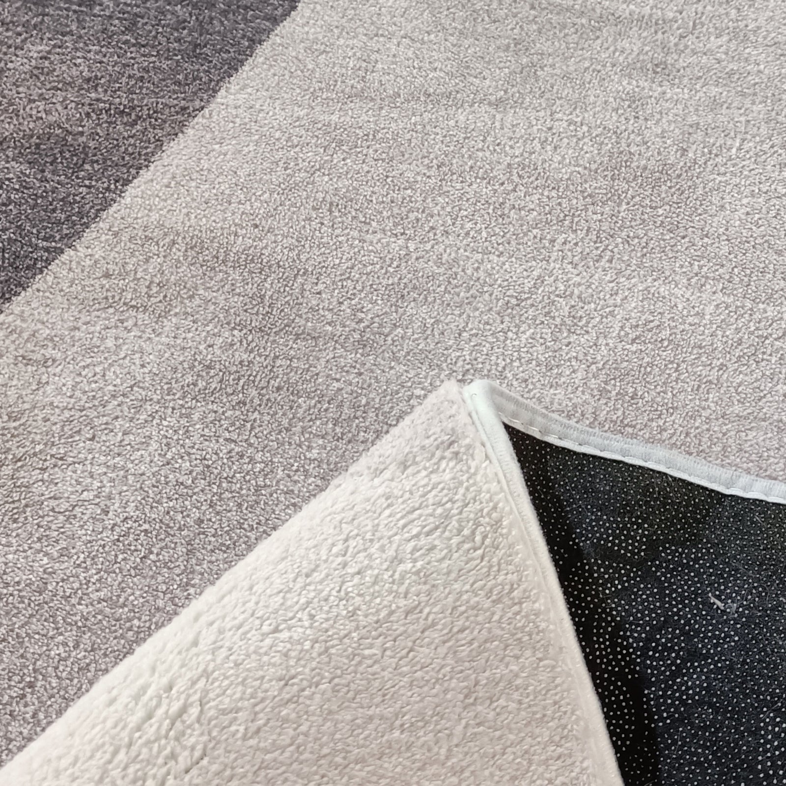 Glote 120x180cm Small Abstract Indoor Floor Rug on grey carpet, corner flipped to show black non-skid backing with white rubberized dots, showcasing its textured surface and subtle abstract leaf pattern.