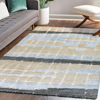 Isaac 200x300cm Abstract Wool Blend Handwoven Shag Rug with a soft grid pattern under a gray tufted sofa, complemented by a potted plant and white ottoman in a modern living room.
