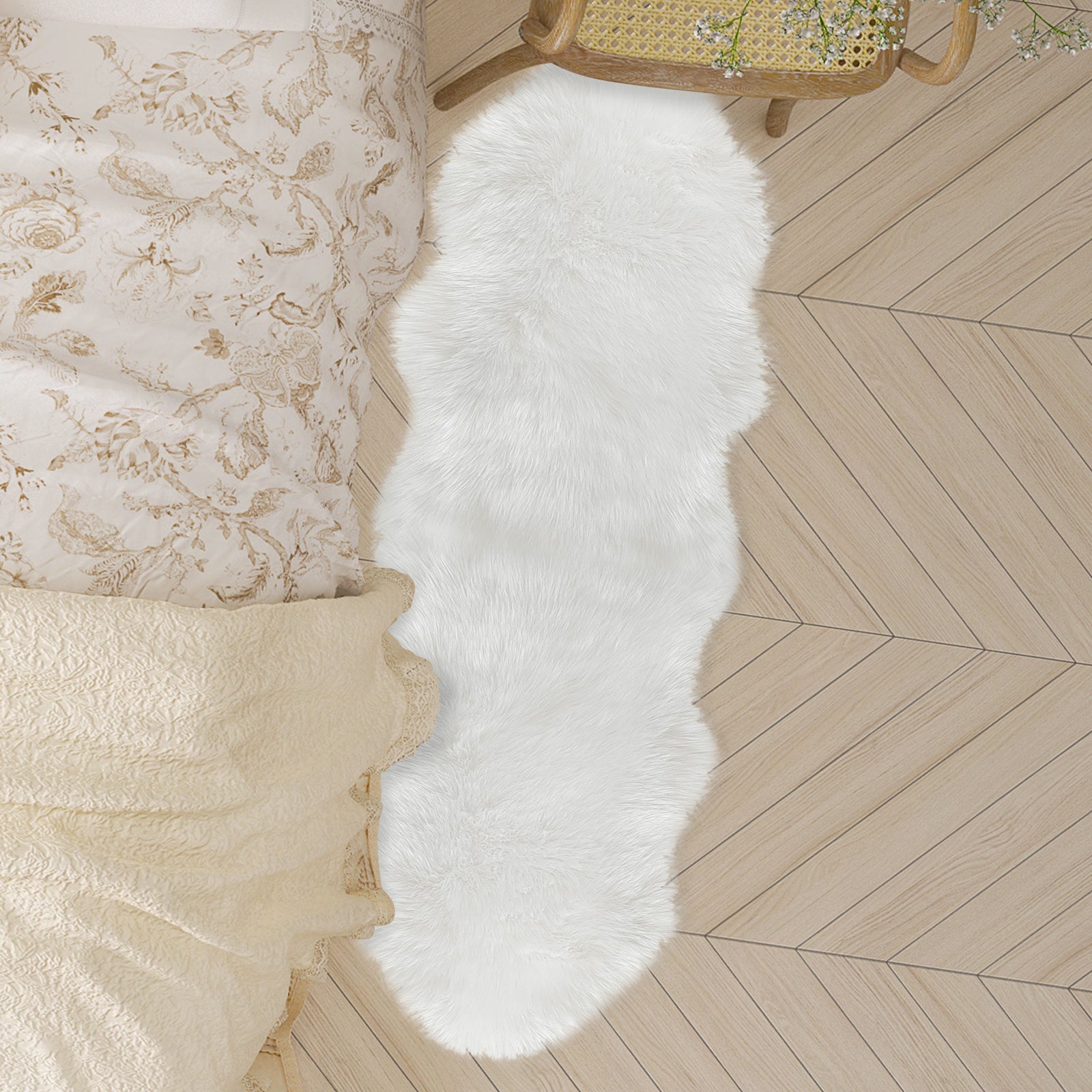 Kalina White Shaggy Fluffy Fur Rug 60x180cm in a cozy bedroom, draped over light wood herringbone floor, beside a cream quilted bed, enhancing warmth and texture with its faux sheepskin appearance.