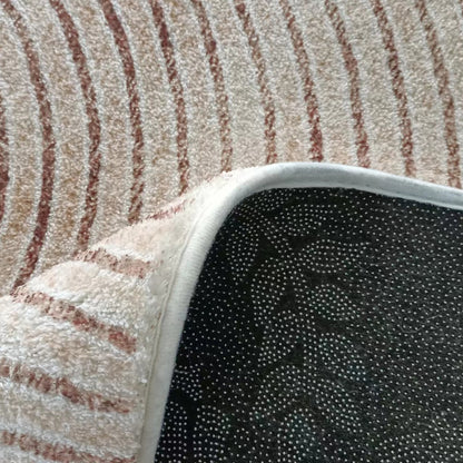 Lunder 160x230cm Modern Abstract Floor Rug with cream-and-light-brown wave stripes, flipped to show black, dotted non-slip backing on a larger carpet.