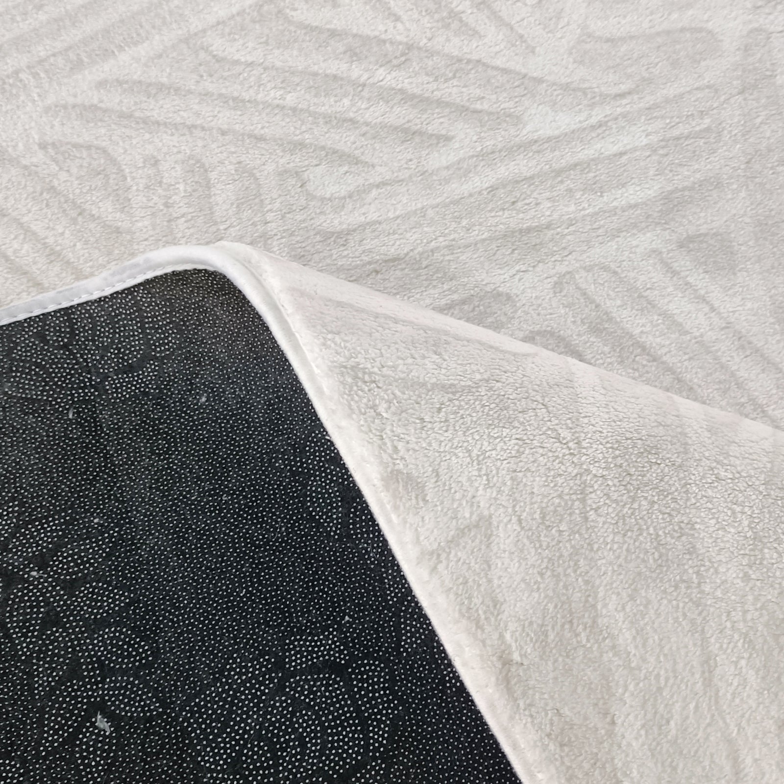 Malung 120x180cm Contemporary Indoor Floor Rug, featuring an off-white plush fabric with a black non-slip backing. The rug's corner is flipped to reveal tiny white grip dots.