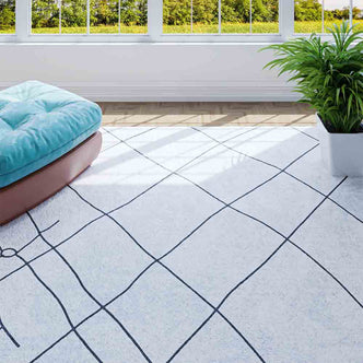 Melody Black and White Modern Floor Rug 200 x 300cm with abstract black grid pattern on ivory, laid in a sunlit room featuring large windows, a blue pouf, and a green plant.