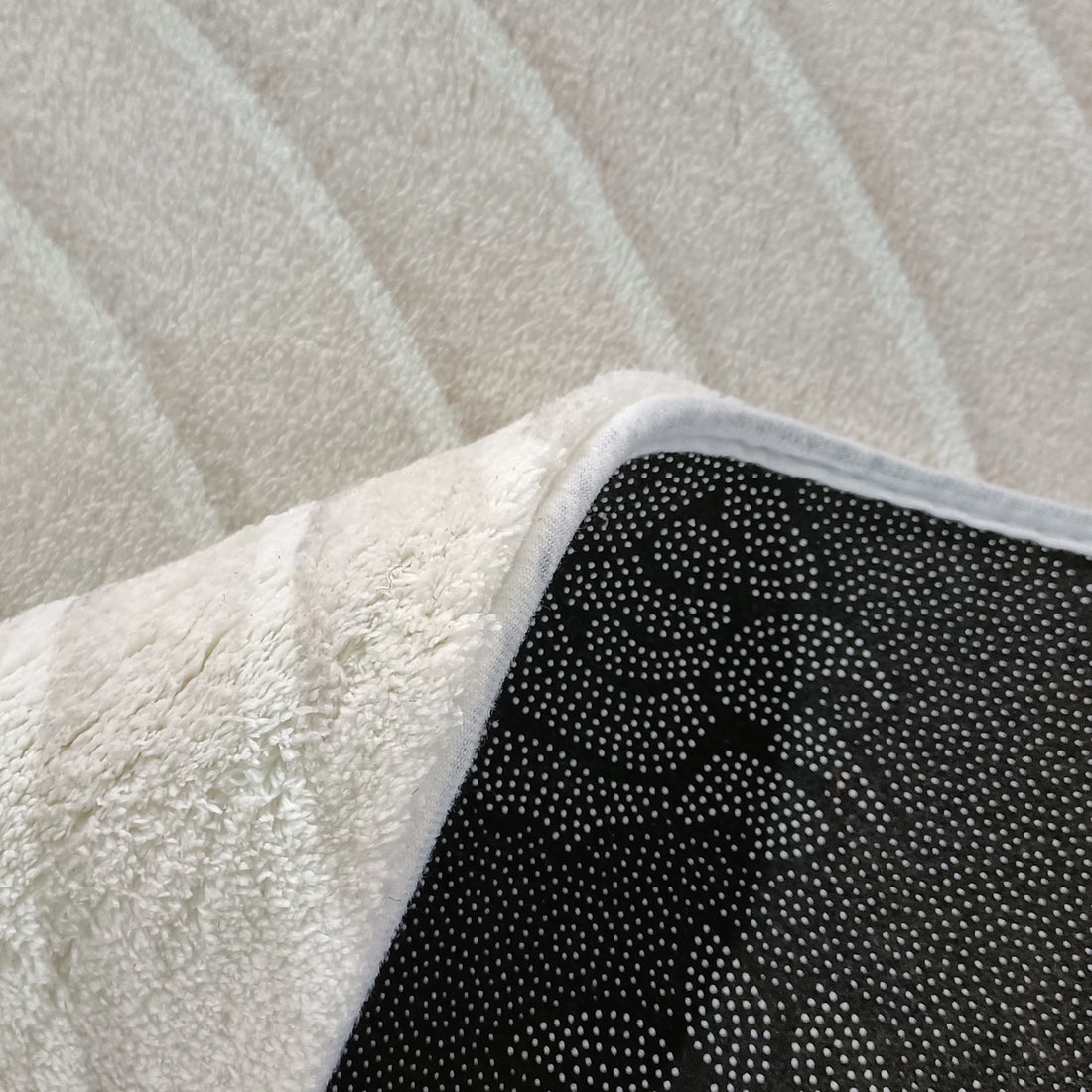 Meraker Modern Abstract Rug 160x230cm flipped to show black non-slip backing with white dots, featuring a soft, shaggy white top surface, lying on a light-colored floor.