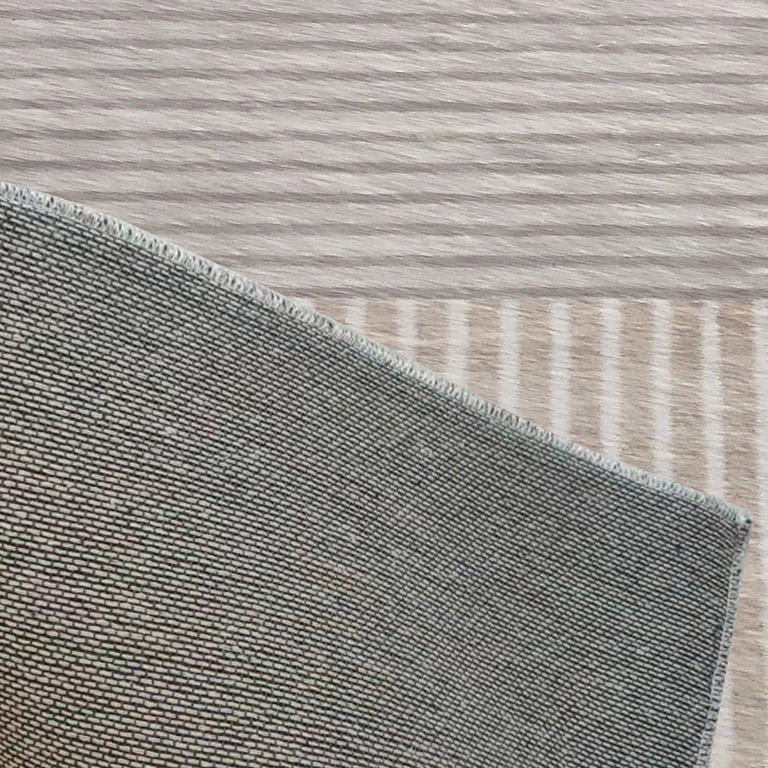 Close-up of the Olivia 160x230cm Polyester Tufted Modern Abstract Indoor Rug showcasing its tightly woven grey pattern and stitched edge on a light wood surface.