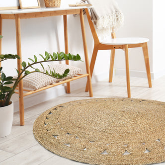 Ophelia 180cm Round Textured Seagrass Indoor Rug in Natural, featuring a braided design with a simple scalloped border, lies in a Scandinavian-inspired, minimalist room setting.