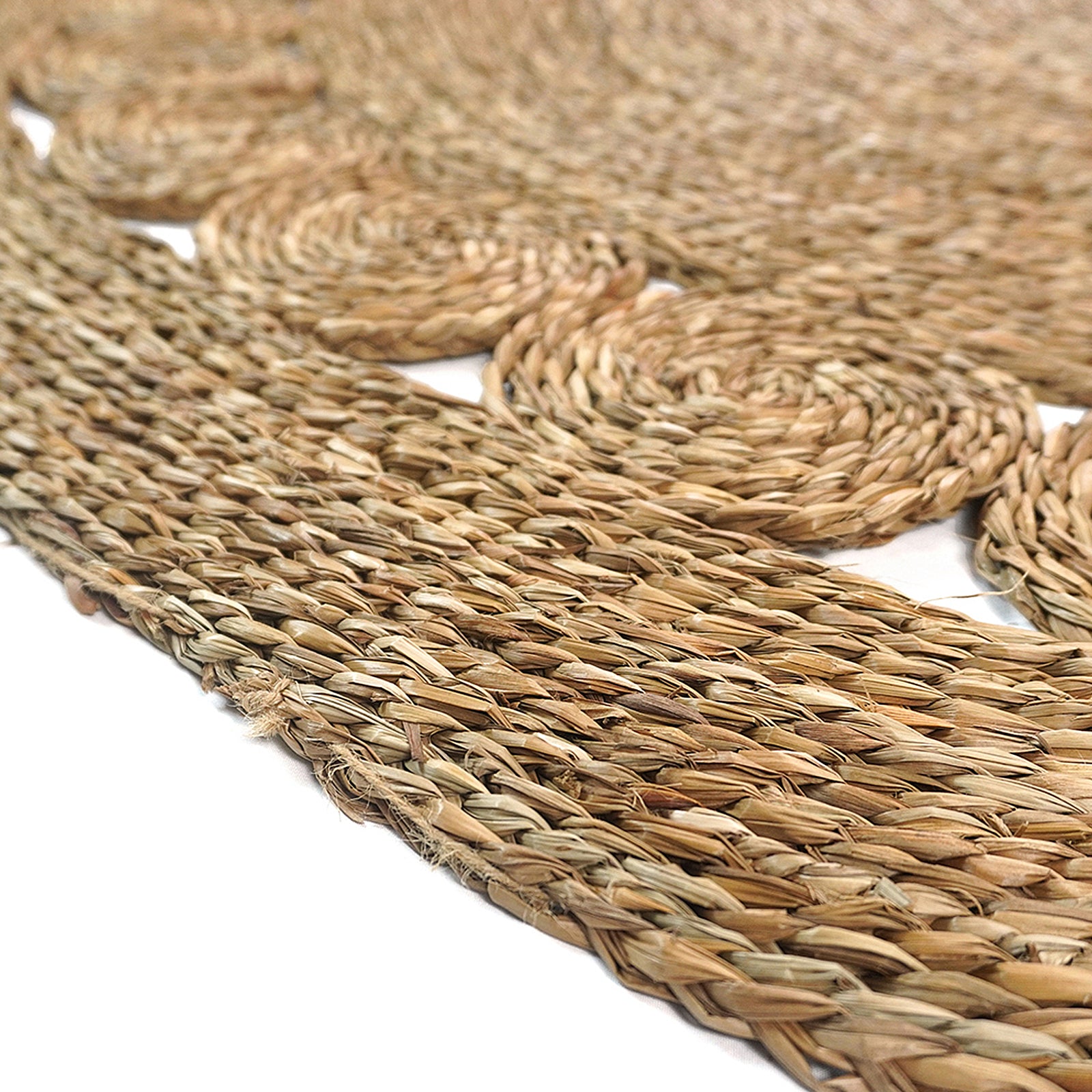 Close-up of the Ophelia 180cm Round Textured Seagrass Indoor Rug in Natural, featuring braided coils of seagrass woven into circular motifs, resembling a rustic, handmade aesthetic.
