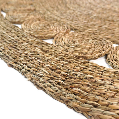 Close-up of the Ophelia 180cm Round Textured Seagrass Indoor Rug in Natural, featuring braided coils of seagrass woven into circular motifs, resembling a rustic, handmade aesthetic.