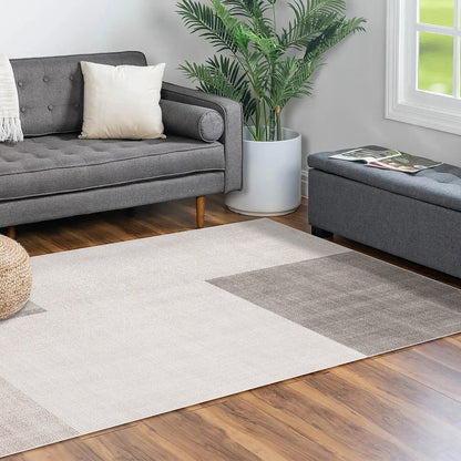 Orsa 200x300cm Small Contemporary Indoor Floor Rug on warm wood-tone floor, featuring a modern design with neutral tones. Complements a gray sofa and ottoman, enhancing the room's modern elegance.