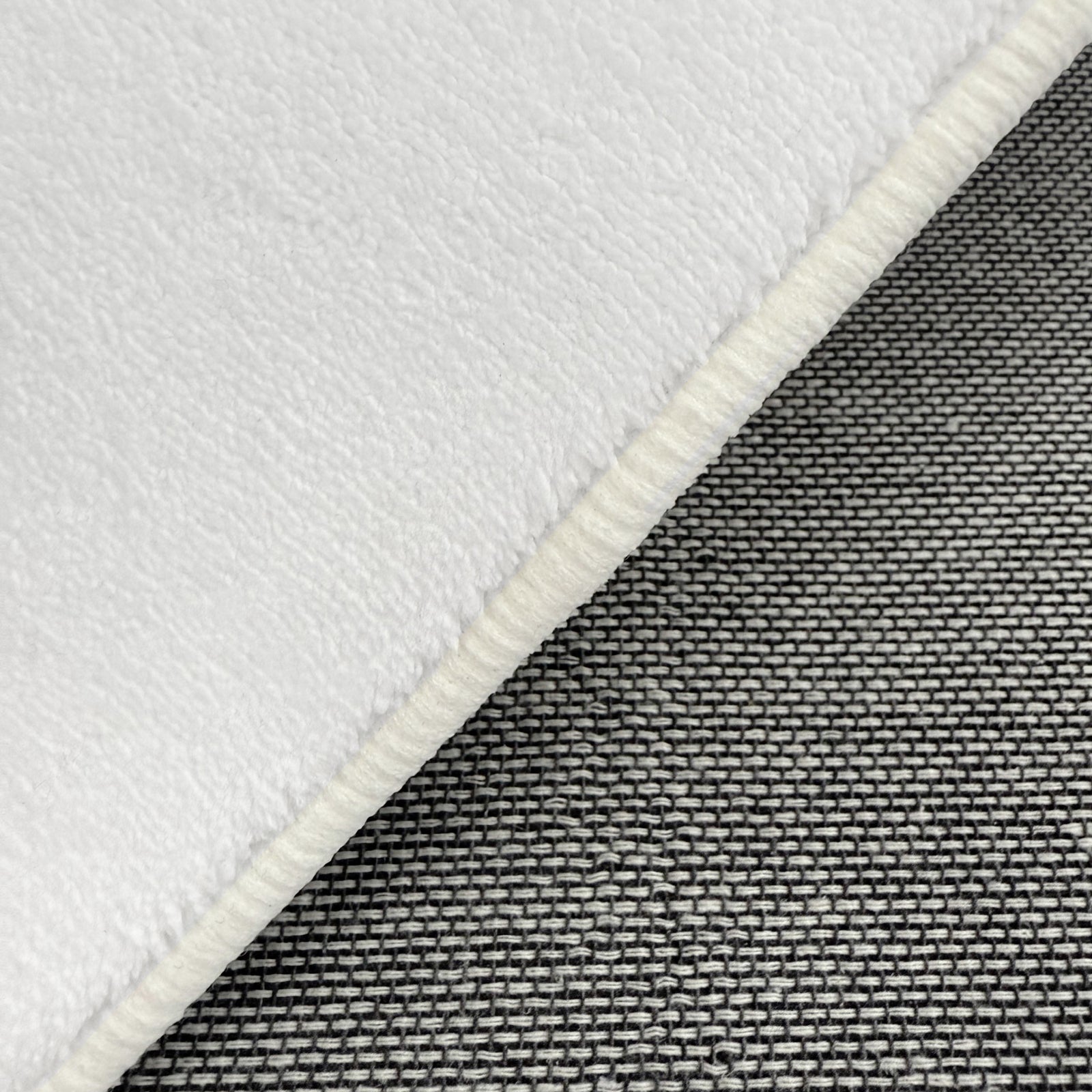 Close-up of Parna 200 x 300cm Curved Shaggy Rug in Cream White, showcasing soft, fleecy texture with overlocked border, layered over tightly woven gray fabric for contrast.