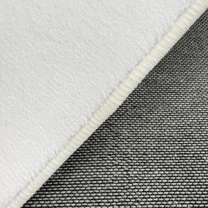 Close-up of Parna 200 x 300cm Curved Shaggy Rug in Cream White, showcasing soft, fleecy texture with overlocked border, layered over tightly woven gray fabric for contrast.