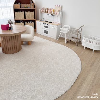 Pavla 200 x 300cm Oval Soft Rug in Cream White lays elegantly in a playroom corner, complementing the white play kitchen and child-size furniture, enhancing the room's cozy, modern aesthetic.