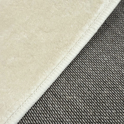 Close-up of Pavla Oval Shaggy Rug - Beige, showcasing its plush, cream fabric with stitched edge alongside a contrasting gray, coarse, basket-weave texture, highlighting the rug's luxurious, soft texture.