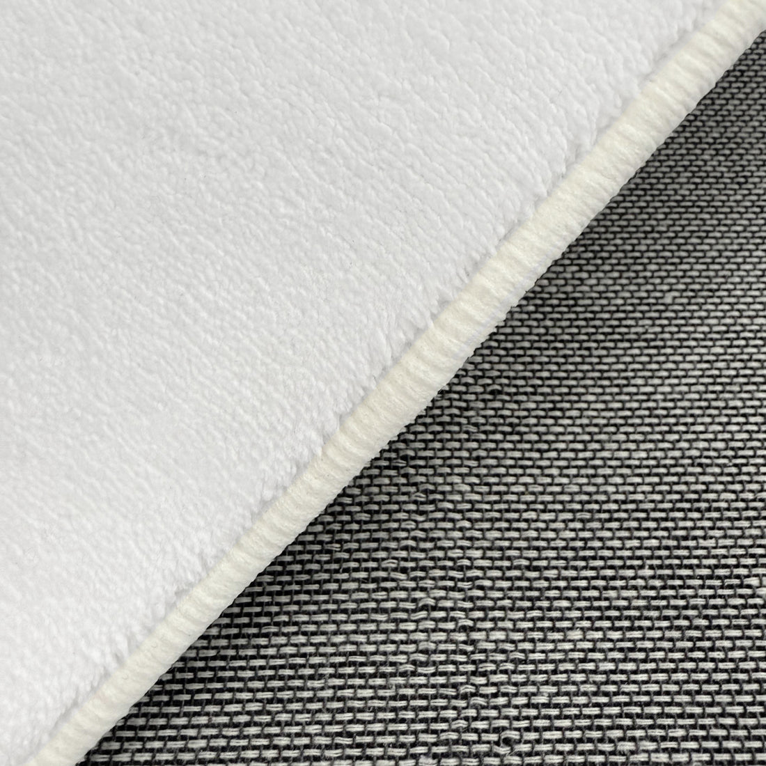 Close-up of Pavla 300 x 400cm Oval Shaggy Rug in Cream White, showing its fleecy texture atop a grey-and-white woven fabric, highlighting the rug's plush, inviting surface.