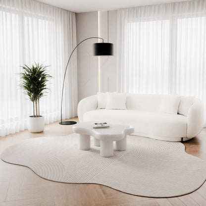 Penina 200 x 300cm Cloud Soft Rug in Neutral beneath a white coffee table, featuring an irregular shape and subtle linear patterns, harmoniously blending with a plush, curved white sofa in a minimalist living room.