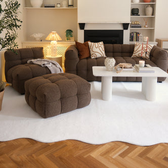 Pixie 200x300cm Large Wavy Soft Rug in Cream White under a tufted brown lounge chair, ottoman, and coffee table in a cozy living room, highlighting its plush texture and elegant wavy design.