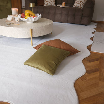 Pixie 240x330cm Large Wavy Soft Rug in Cream White, featuring an organic, wavy edge, displayed in a cozy living room with floor cushions, a coffee table, and decorative items.