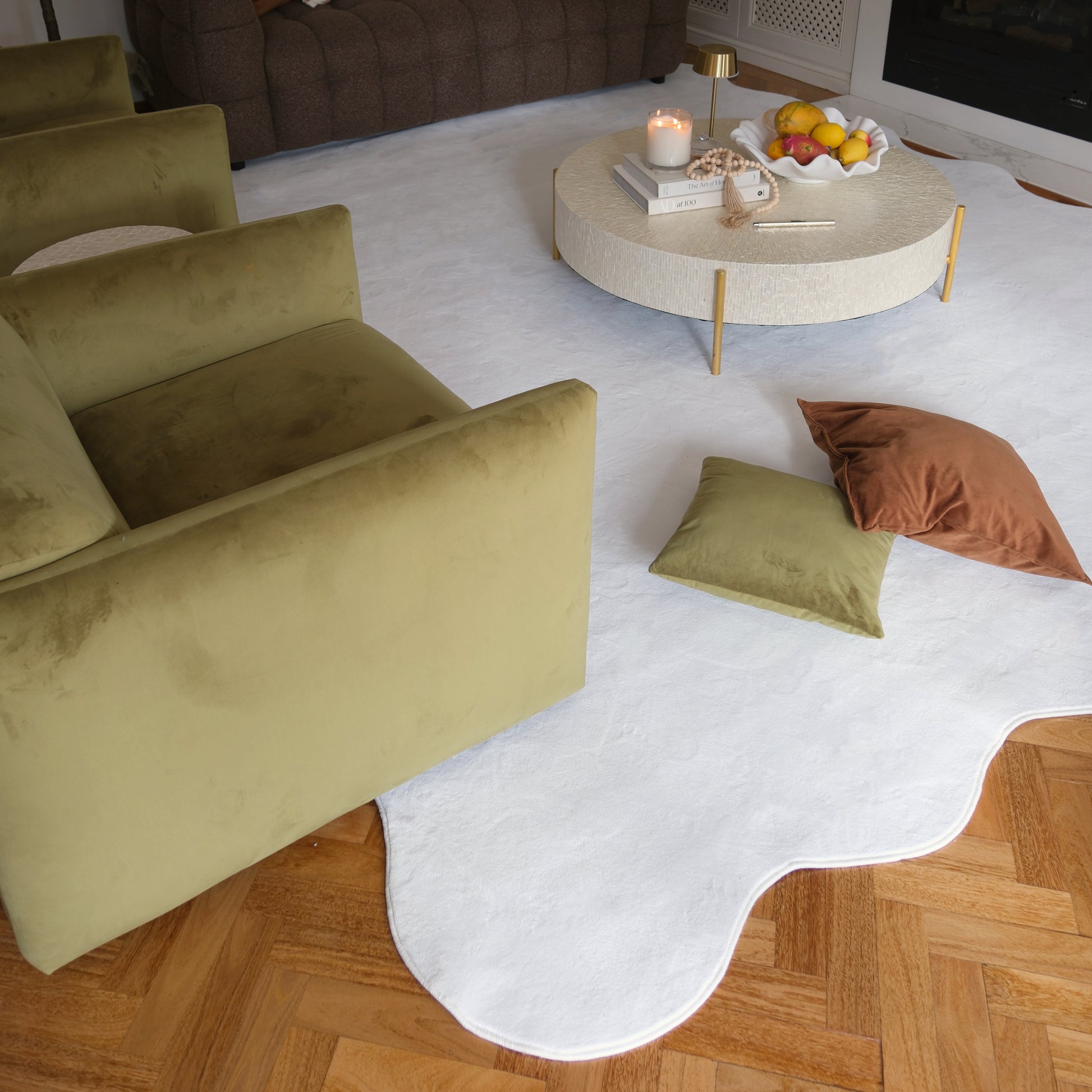 Pixie 300x400cm Large Wavy Soft Rug in Cream White lies on herringbone wood floor, with a round coffee table and an olive-green sofa nearby. The rug's abstract shape adds elegance.