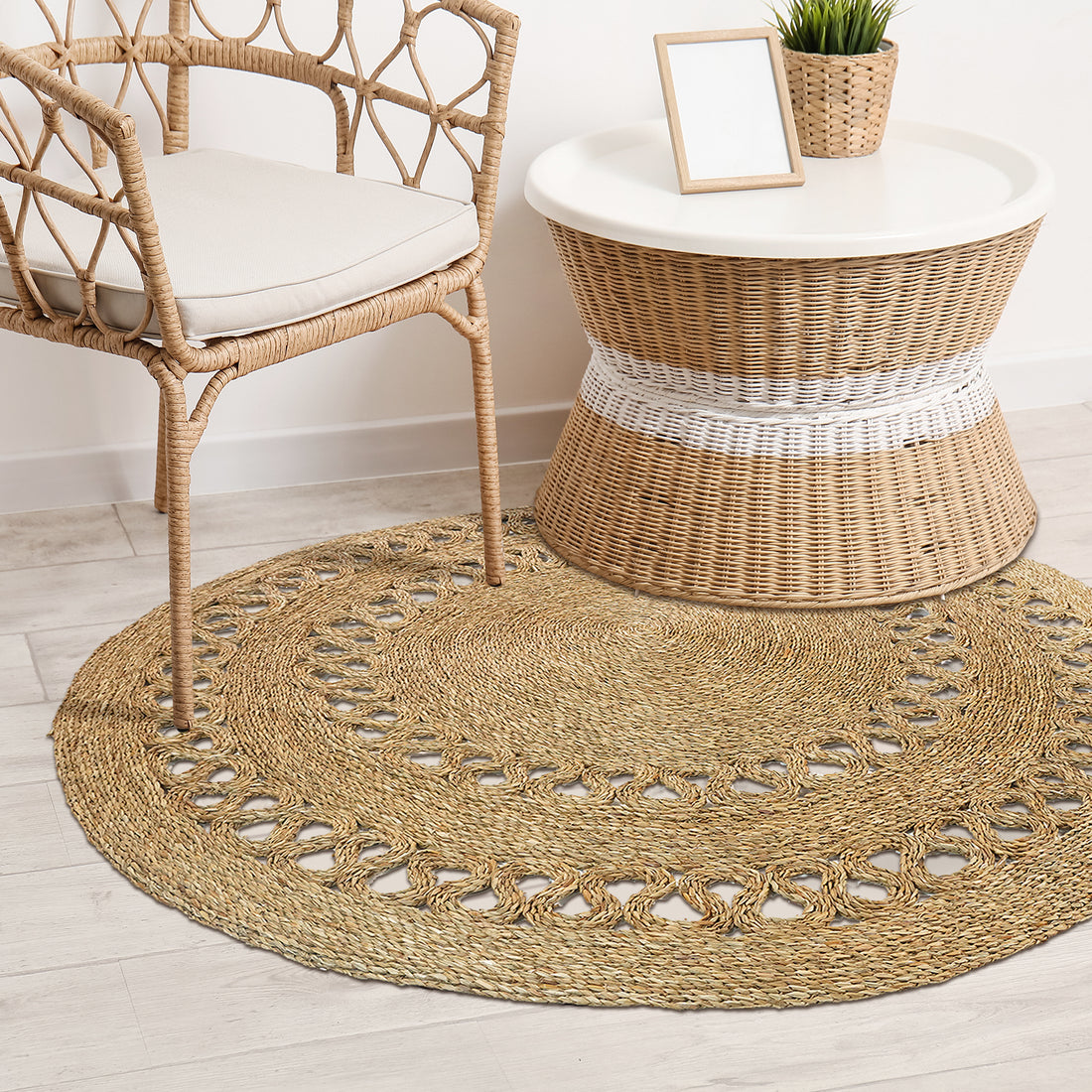 Sandra Brown Seagrass Rug 180cm, featuring intricate braided design and decorative looped edging, complements a minimalist boho interior with a rattan armchair and wicker side table arrangement.