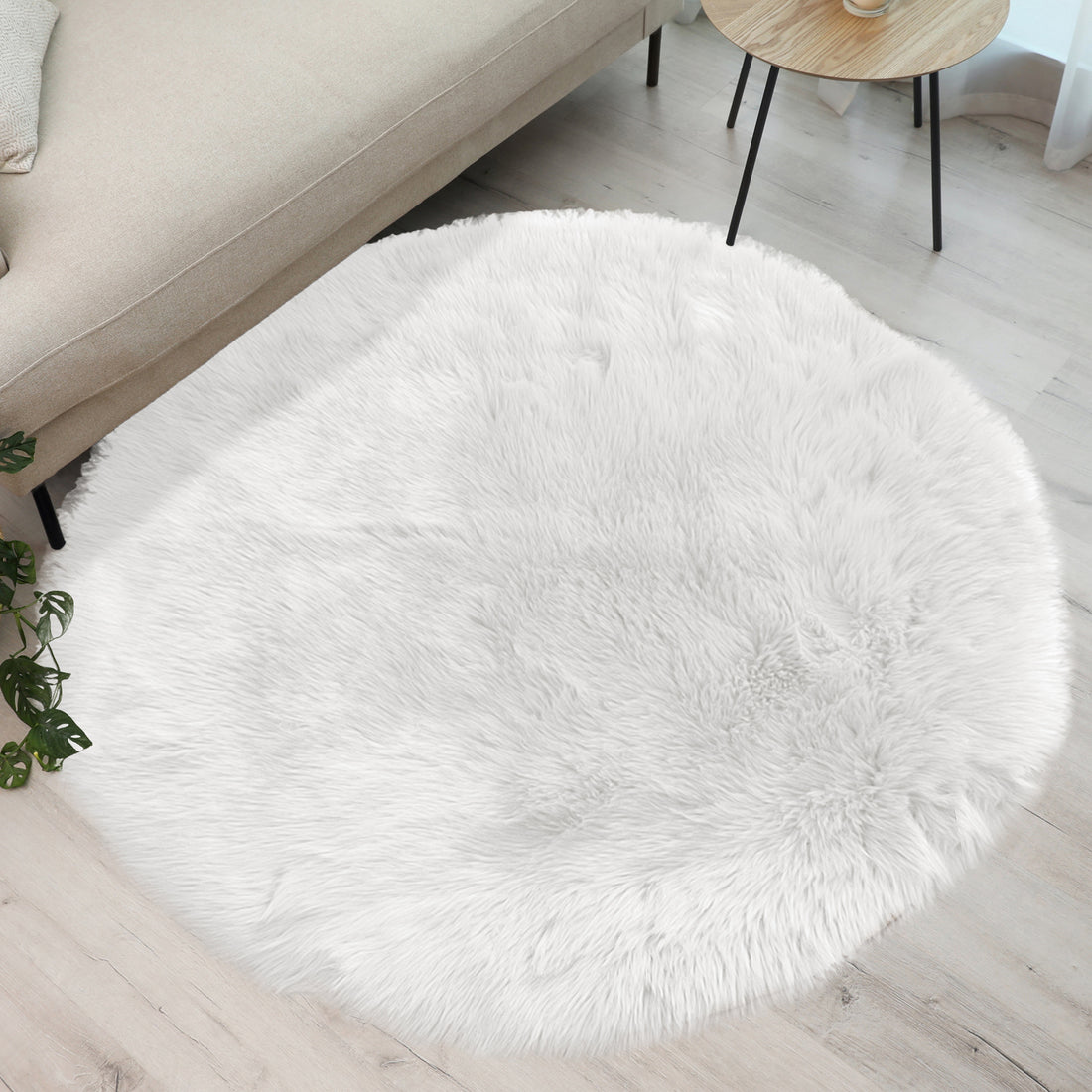 Shaddi 120cm Round Shaggy Soft Fluffy Fur Rug in White on wood floor, next to beige sofa and small wooden table, enhances the modern living-room corner with plush texture and cosy elegance.