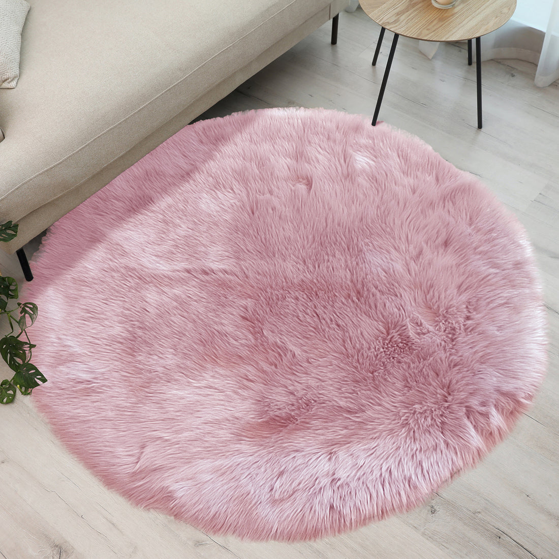 Shaddi 160cm Round Shaggy Soft Fluffy Fur Rug in Pink lies under a beige sofa, enhancing a cozy living room with its plush texture and luxurious faux fur look.