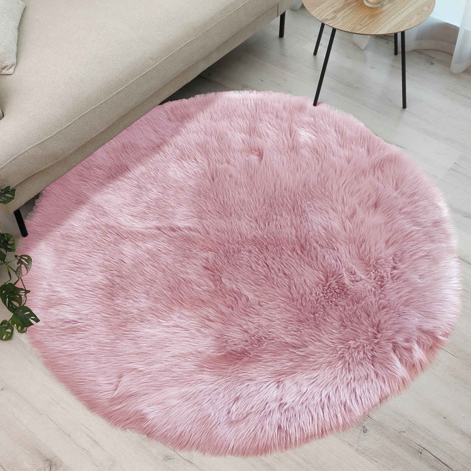 Shaddi 160cm Round Shaggy Soft Fluffy Fur Rug in Pink lies under a beige sofa, enhancing a cozy living room with its plush texture and luxurious faux fur look.