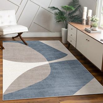 Sharya 160x230cm Abstract Indoor Floor Rug with overlapping-arc pattern in blue, beige, and off-white, placed in a modern room, complemented by a console, lounge chair, and potted plants.