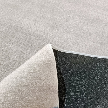 Sharya 200x300cm Abstract Indoor Floor Rug on a light-gray carpet, with one corner flipped showing black non-slip backing with white grip-dot patterns, highlighting its functional design.