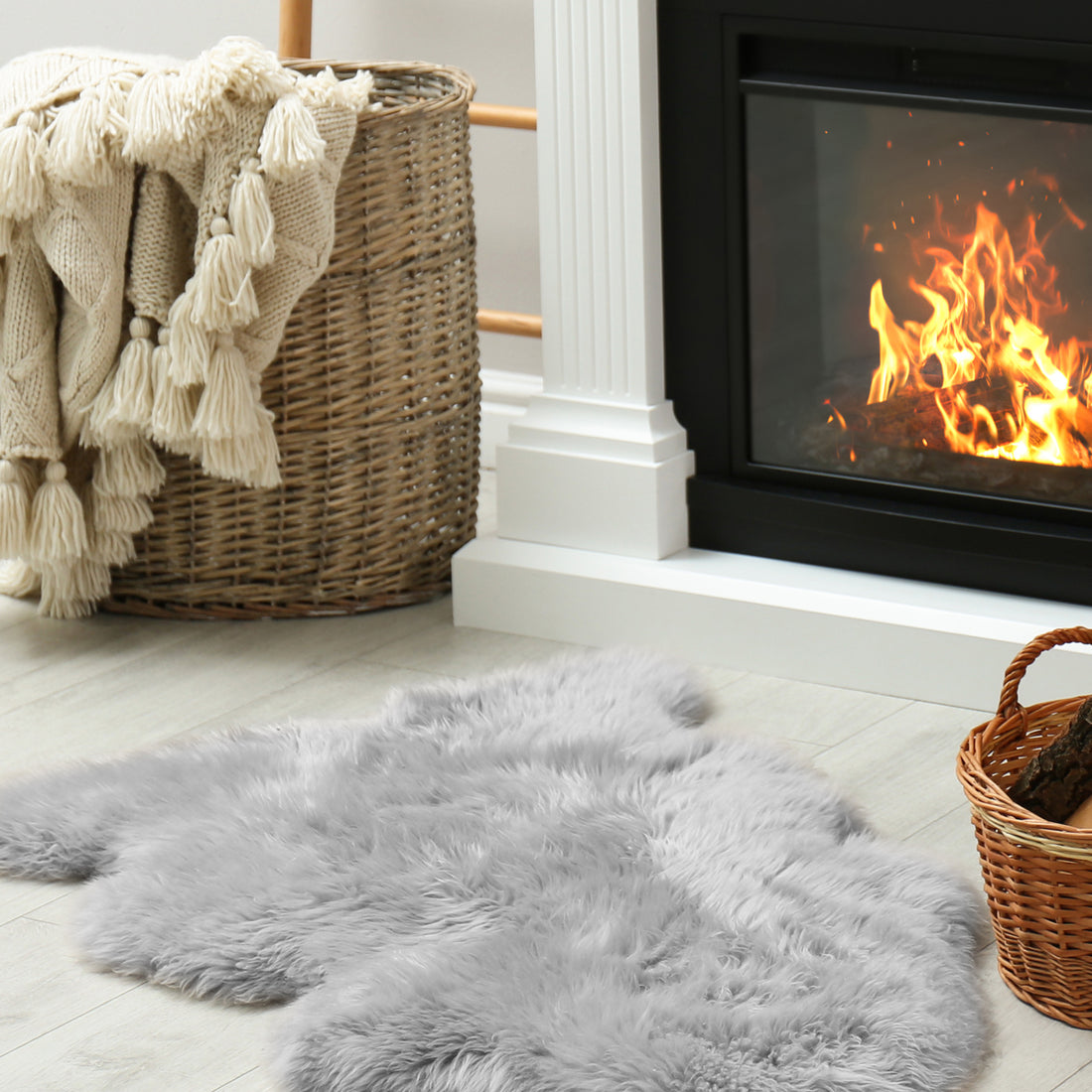 Silvanus 60x90cm Shaggy Soft Fluffy Fur Rug in Grey lies on a pale wood floor beside a wicker basket with a knit throw, near a small basket of firewood by the fireplace.