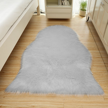 Silvanus 60x90cm Shaggy Soft Fluffy Fur Rug in Grey, plush and faux-fur, lies on light-wood flooring, beside a white bed frame and cream dresser, enhancing the cozy bedroom corner.