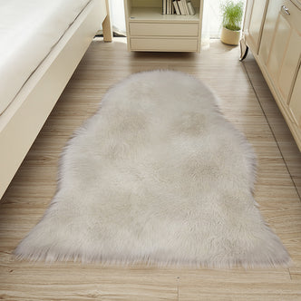 The Silvanus 60x90cm Shaggy Soft Fluffy Fur Rug in Tan & White is displayed in a light-filled bedroom corner, enhancing the wood-grain floor with its plush, faux-fur texture.