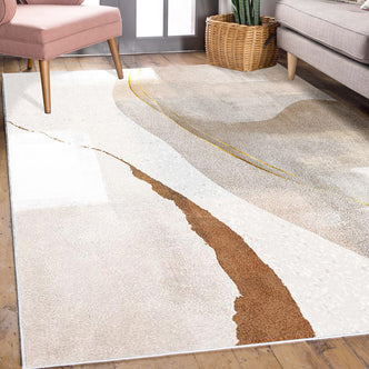 Talbyn Contemporary Abstract Floor Rug 120 x 180cm featuring sweeping cream, tan, and gray patterns with a rust-colored accent, set on a wood floor, partially surrounded by a pink chair and gray sofa.
