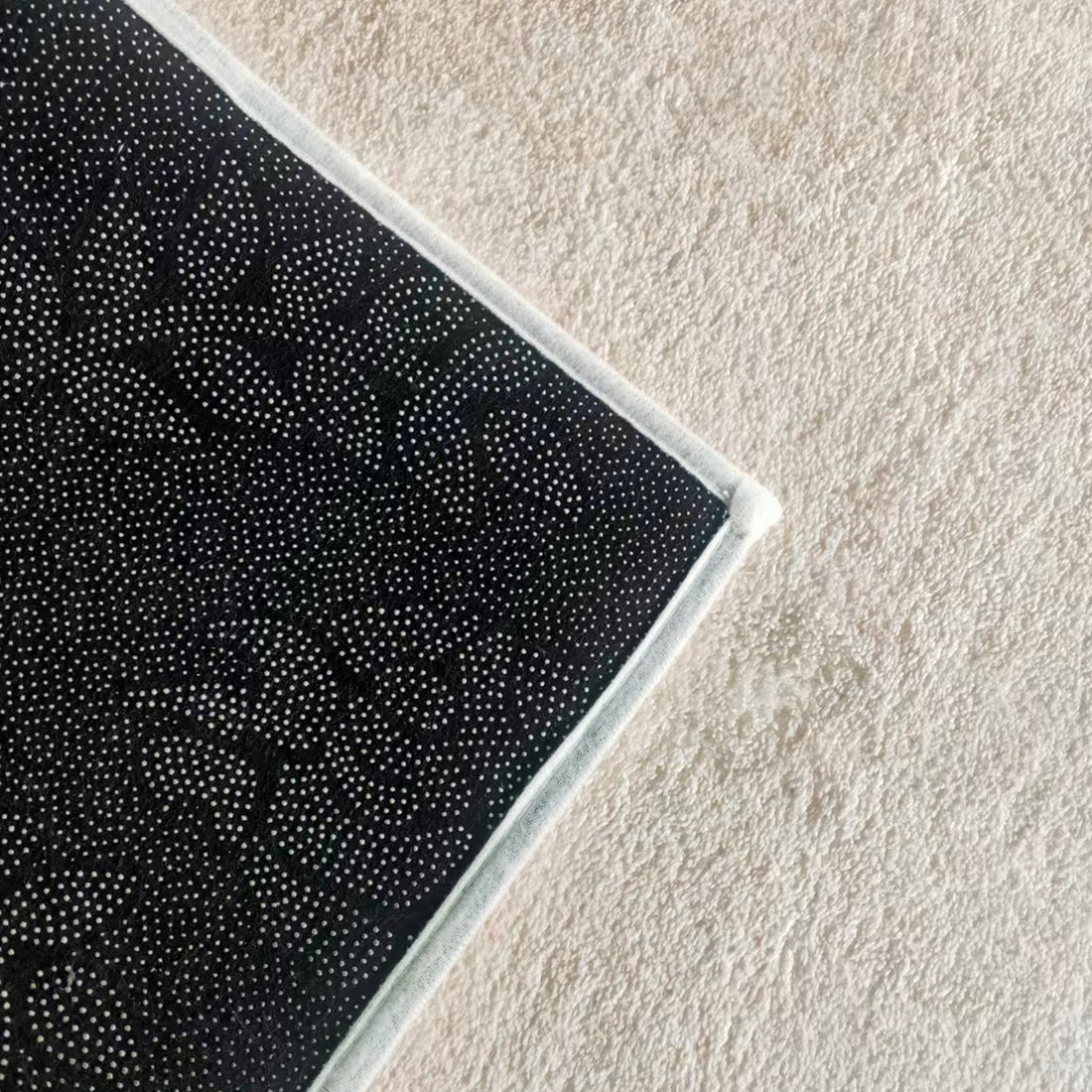 Close-up of Talbyn 160x230cm Medium Contemporary Abstract Floor Rug, showcasing a mandala-style pattern and white-stitched border on dark fabric, resting on a light, textured surface.