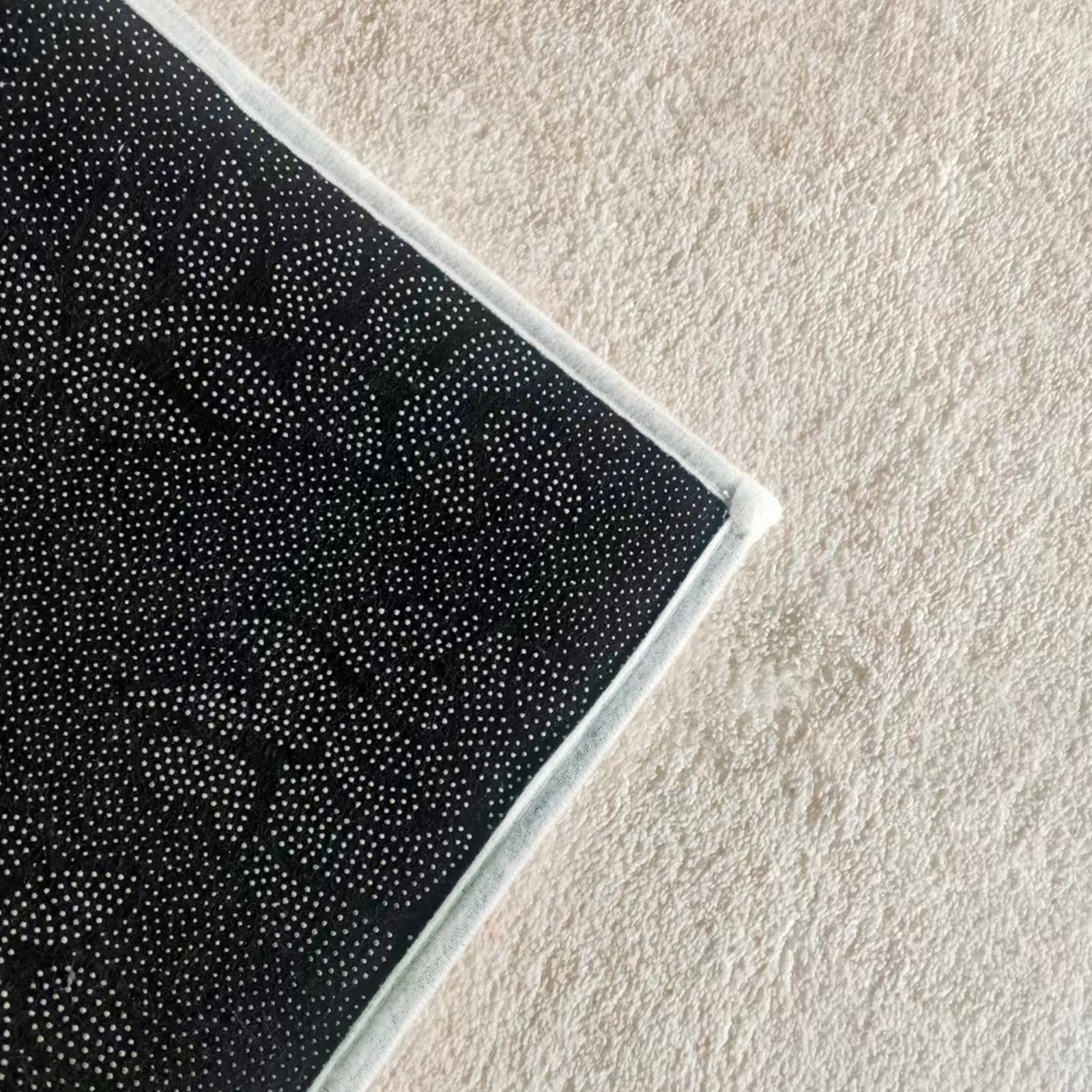 Corner of the Talbyn Contemporary Abstract Floor Rug 200 x 300cm, showcasing a non-slip silicone-dot pattern and white stitched border, lying on a light-colored carpet.