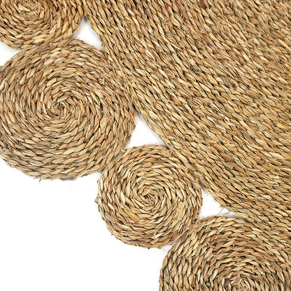 Una 180cm Round Textured Seagrass Indoor Rug in Natural, featuring a handmade spiral-braided design with overlapping circular pieces, displayed against a white background, highlighting its intricate and unique craftsmanship.