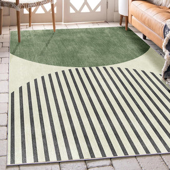 Vannebo Modern Abstract Floor Rug 160 x 230cm with a green semicircle top and striped bottom, set in a living room beside a tan leather sofa and woven chair near French doors.