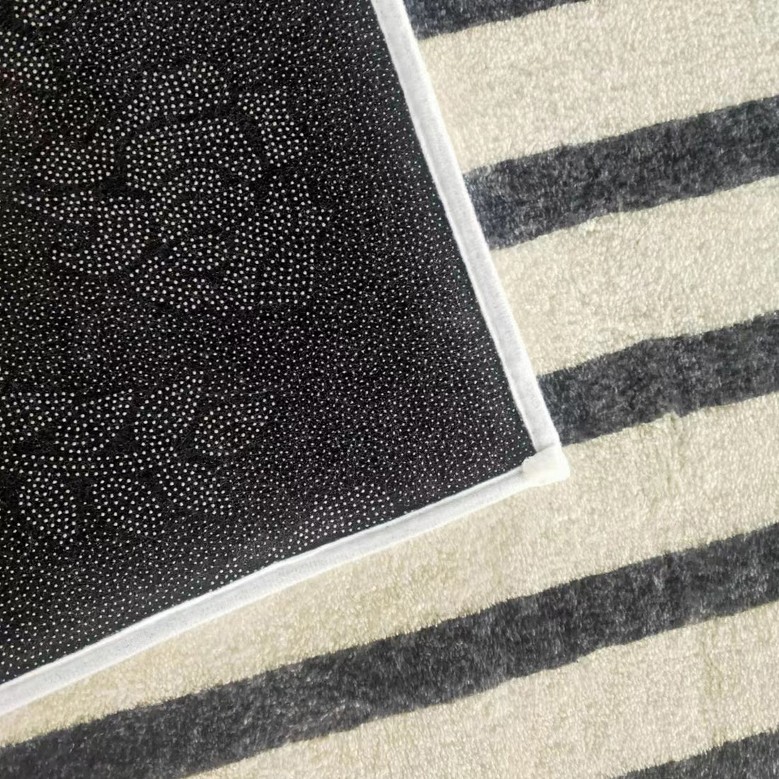Vannebo Modern Abstract Floor Rug 160 x 230cm, showing corner with black dot-grip backing on a striped gray floor.