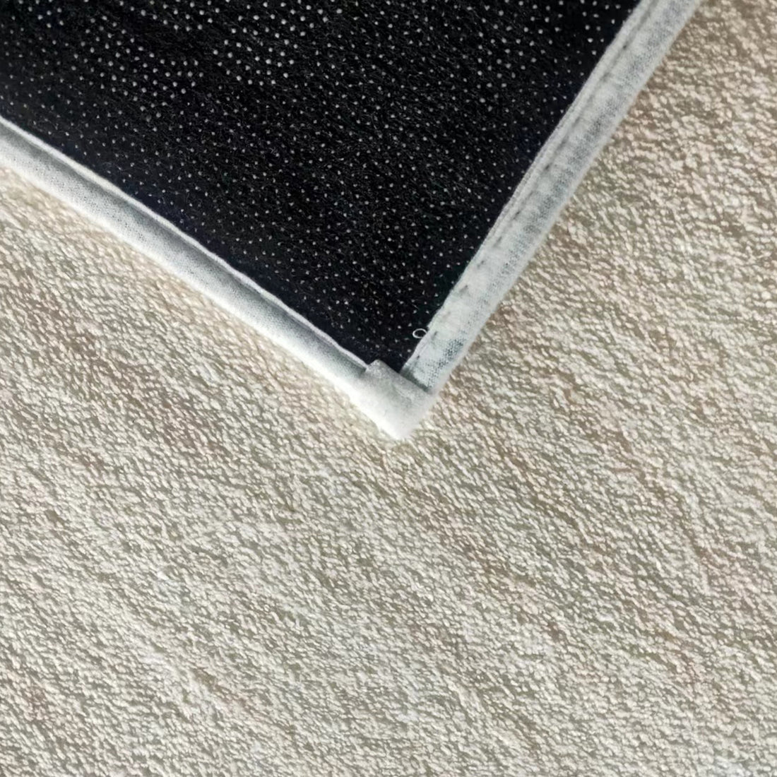 Vastra Modern Abstract Floor Rug 160 x 230cm features a black, rubber-dotted non-slip backing with white fabric edging, shown close-up on a beige textured carpet, highlighting its secure and modern design.