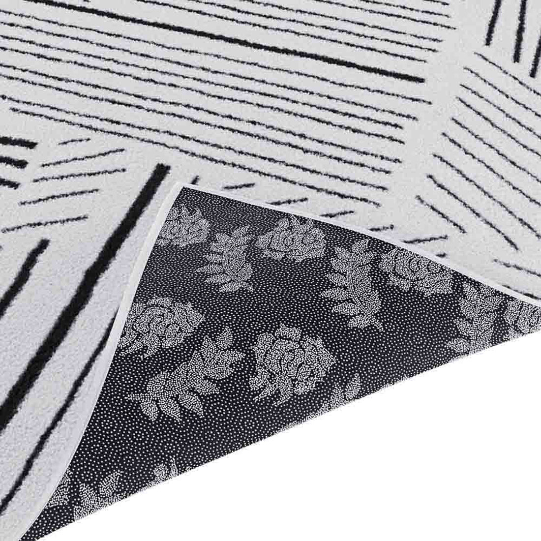 Vikki 120x170cm Small Abstract Contemporary Floor Rug flipped to show white linear-striped upper side and floral motif underside, highlighting its modern monochrome design and durable construction.