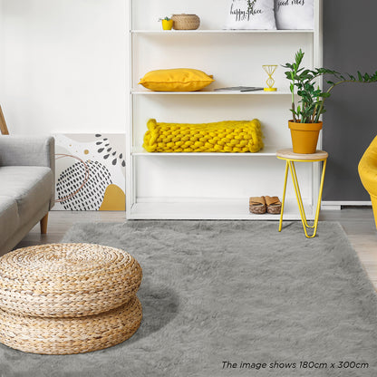 Zubuin 180x300cm Shaggy Plush Rectangular Rug in Grey, displayed in a modern living room setting with a woven rattan pouf, gray sofa, shelving with decor, and yellow accents.