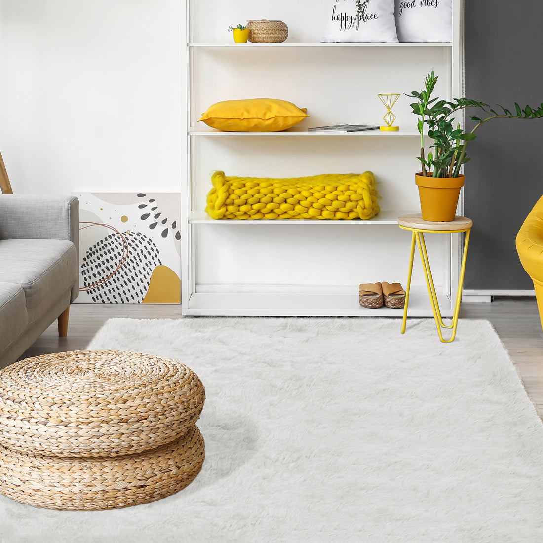 The Zubuin 180x300cm Shaggy Plush Rectangular Rug in White anchors a cozy living room with its soft, luxurious texture, complementing modern decor elements like a round woven pouf and shelving unit.